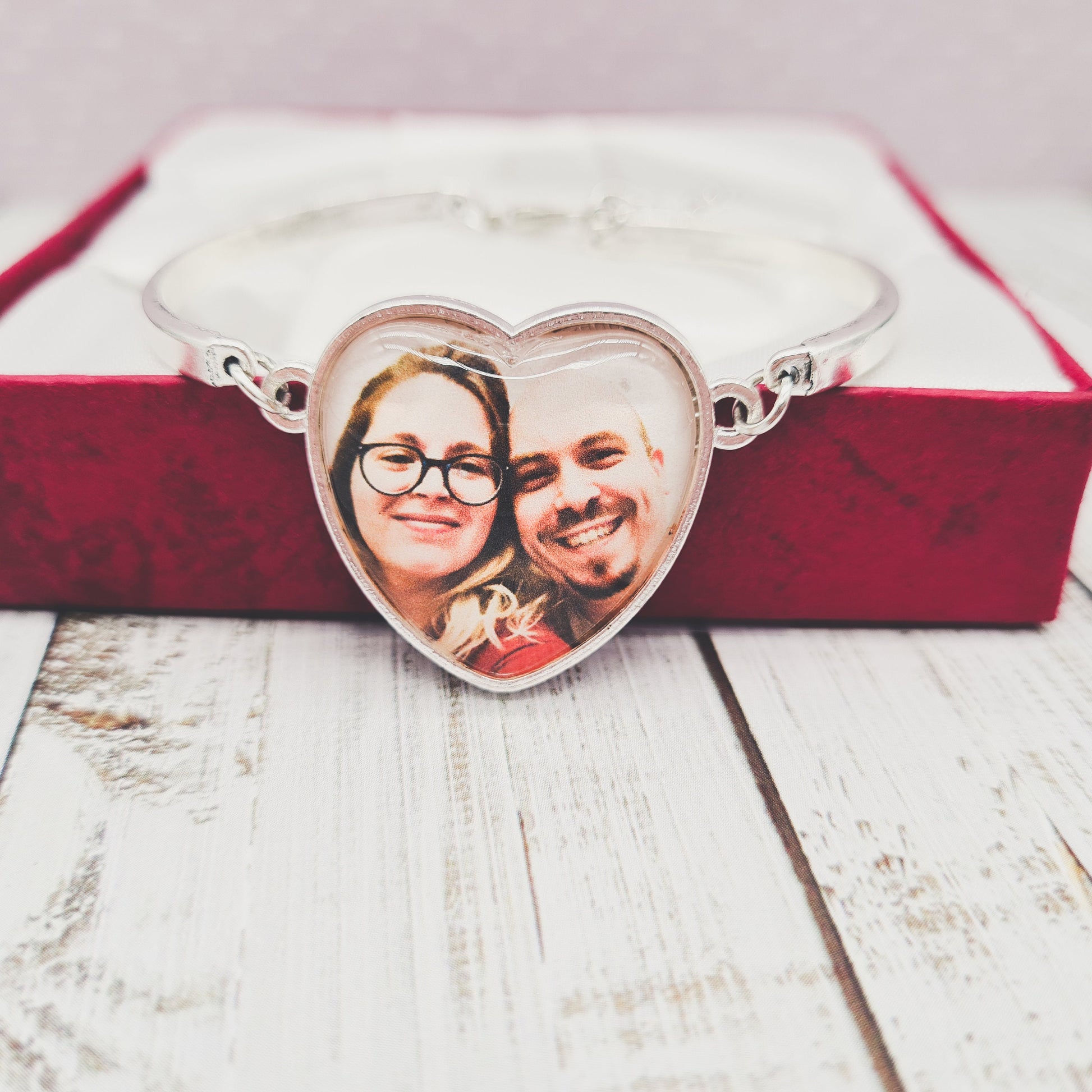 Silver heart shaped bracelet personalised with a photo set in glass in front of a red gift box