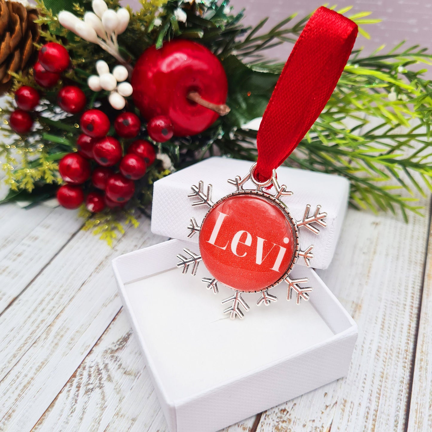 Christmas ornament personalised with a name with red ribbon hanging in Christmas tree