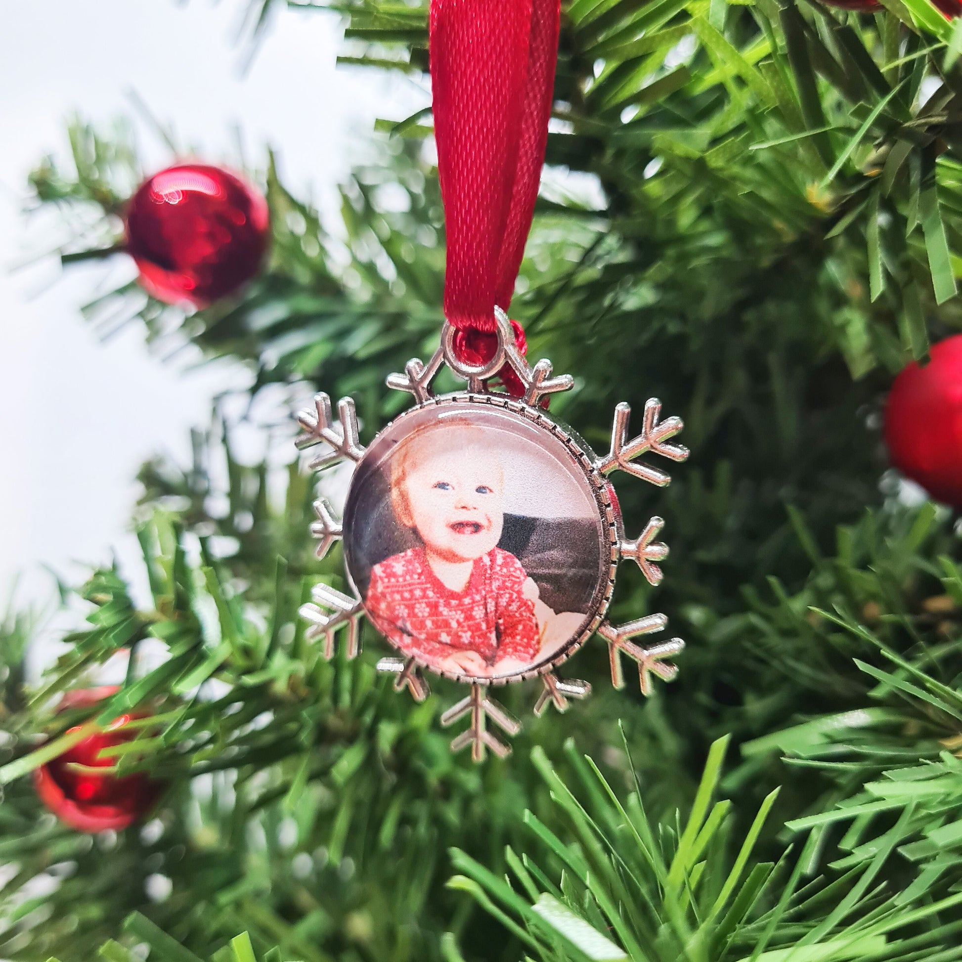 Christmas ornament personalised with photo with red ribbon hanging in Christmas tree