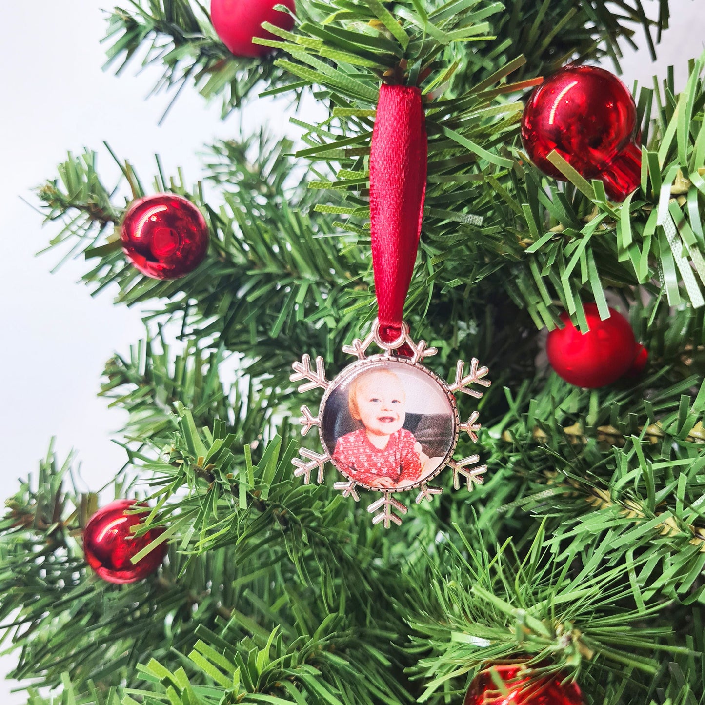 Christmas ornament personalised with photo with red ribbon hanging in Christmas tree